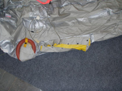 2. Photograph showing the sea anchor pouch as it was found with the stainless steel cable routed through the sill end of the pouch. Note: The yellow arrow points to the single snap that remained snapped