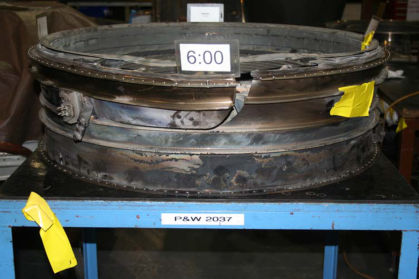 Photo 9: View of tab of displace material on ruptured HPT case (P&W) The upper HPT ACC air duct had the locating bushing broken off. The bracket on the lower HPT ACC air duct was pulled out and remained attached to the upper duct. The lower